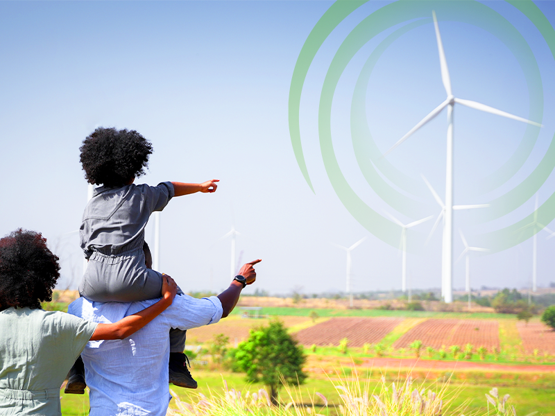 A Black Family comprised of a mother and a father with his daughter on his shoulders is outside looking and pointing at a wind turbine generator with the CGC logo imposed in the sky.